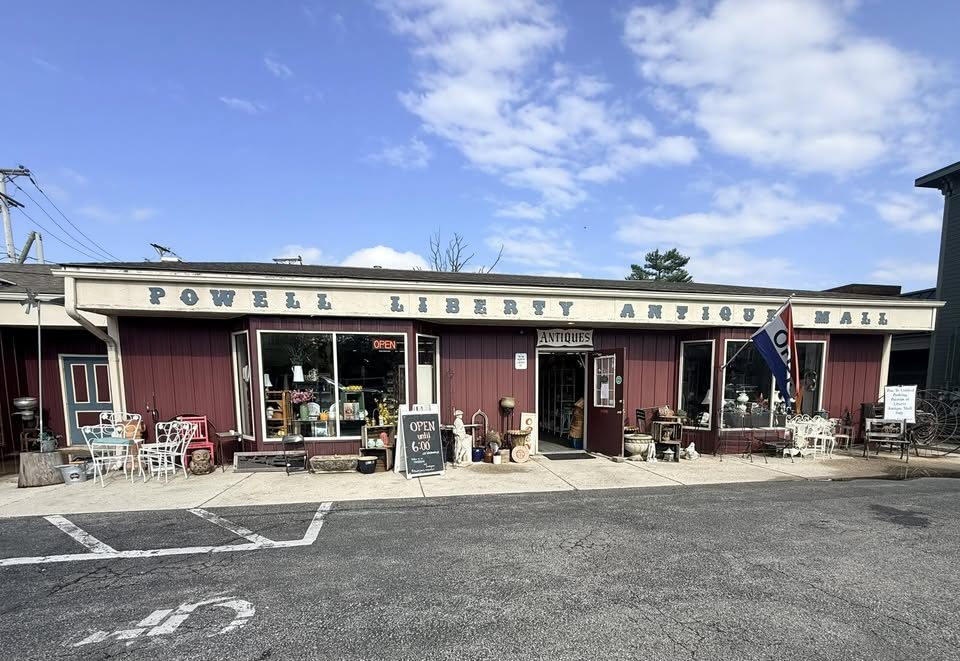 The red storefront of Powell Liberty Antique Mall with vintage furniture displayed out front